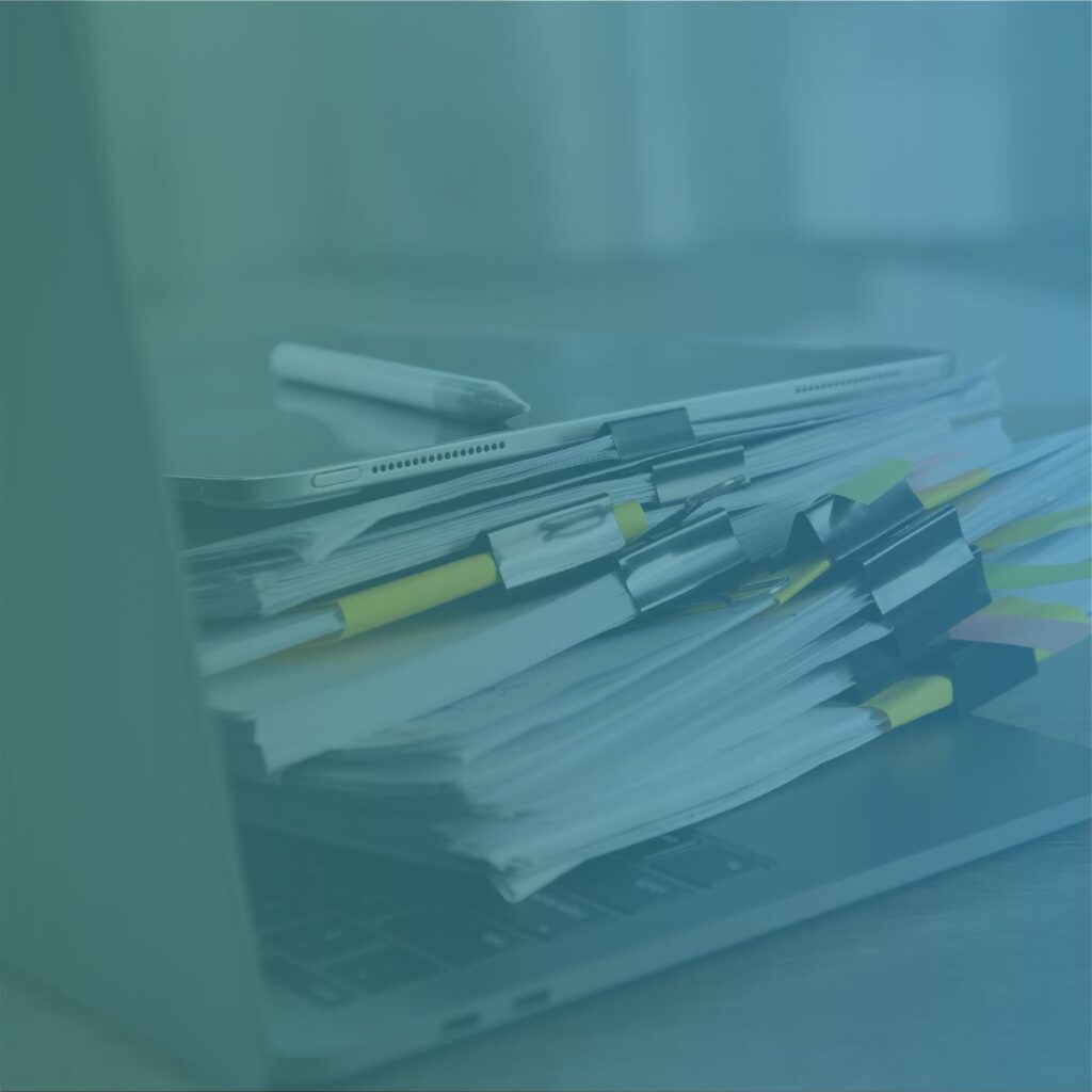 A messy stack of paper contractor timesheets piled on a laptop keyboard representing manual vs digital recruitment back-office processes.
