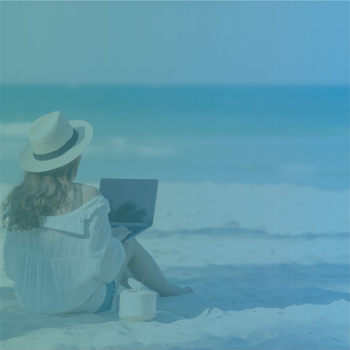 A recruitment agency owner using a laptop on a sandy beach to run a UK business remotely from Spain.